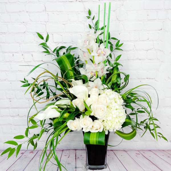 Tall white floral arrangement in a black vase with orchids, calla lilies, and roses