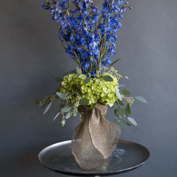Tall blue flower arrangement with green hydrangeas in burlap wrap