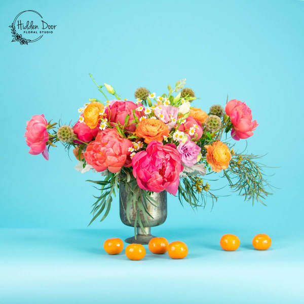 Bright mixed bouquet in a metal vase with oranges on the table