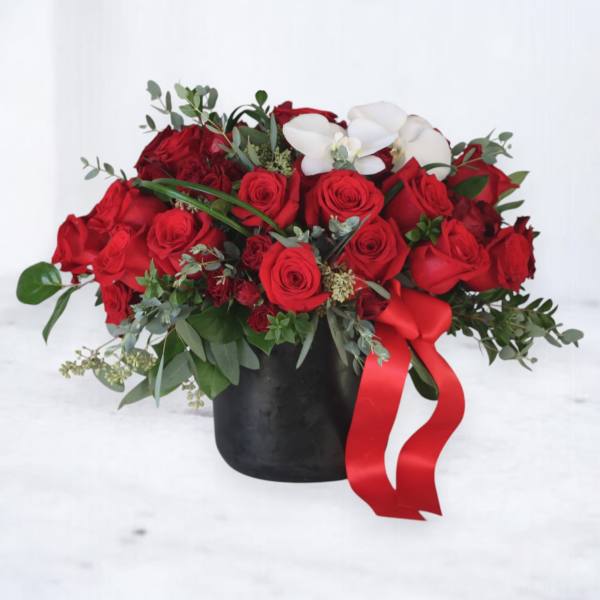 Low black vase of red roses with white orchids and a red ribbon bow