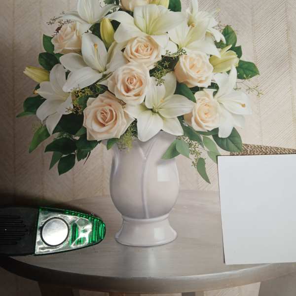 White lilies and pale roses arranged in a white vase