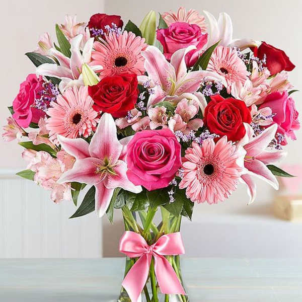 Bouquet of pink and red flowers in a glass vase with a pink ribbon