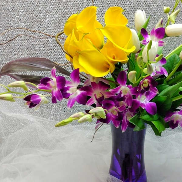 Yellow calla lilies and purple orchids in a purple vase