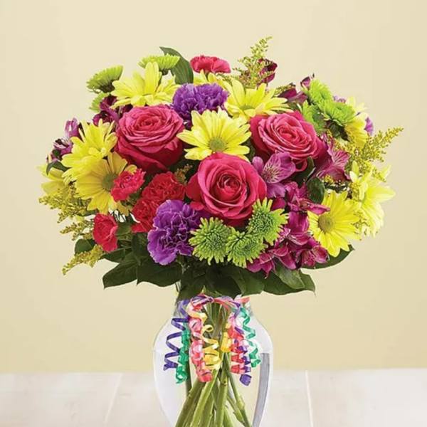 Bouquet of pink roses, yellow daisies, and purple flowers in a glass vase
