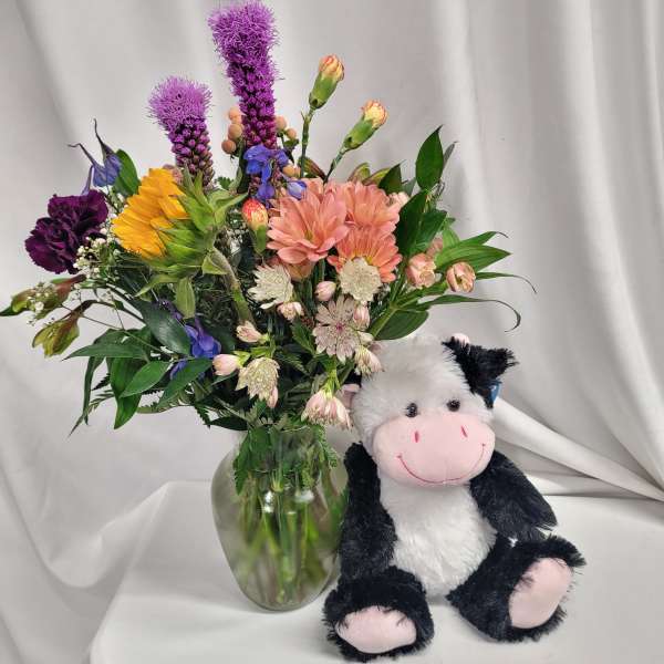 Mixed bouquet in a glass vase beside a plush cow toy