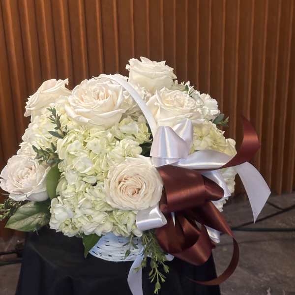 White rose and hydrangea bouquet in a basket with satin ribbons