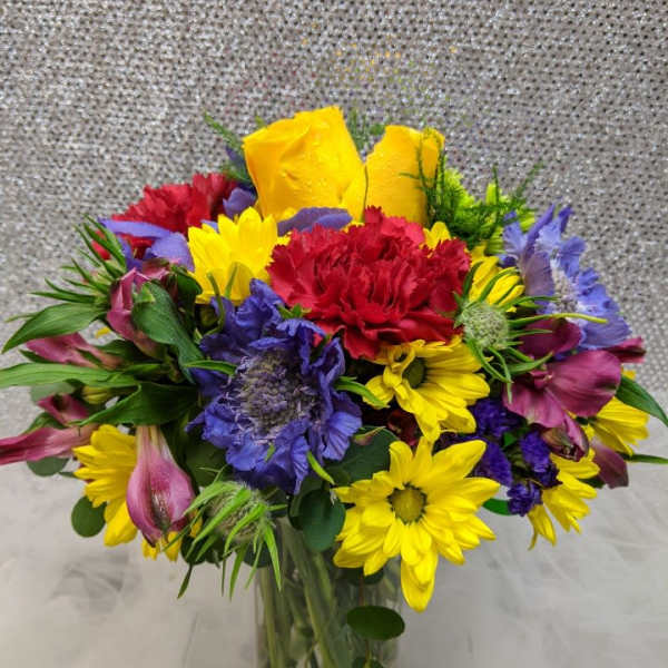 Colorful mixed bouquet in a clear glass vase with yellow, red, purple, and pink blooms