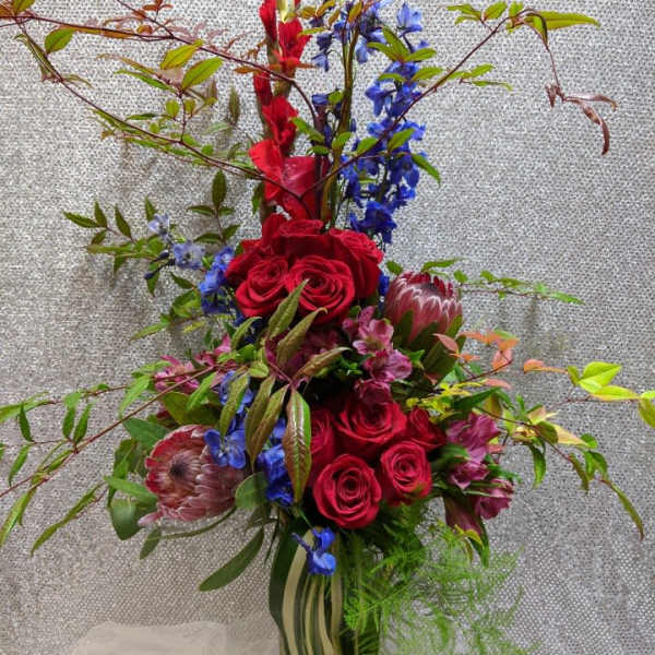 Tall bouquet of red roses, blue flowers, and protea in a glass vase
