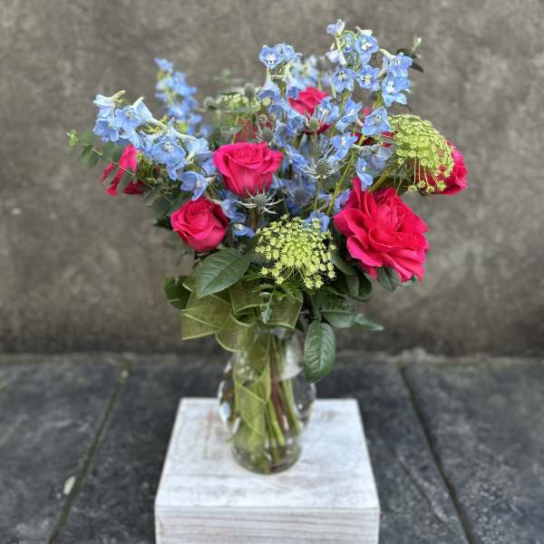 Pink roses and blue flowers in a glass vase with a ribbon