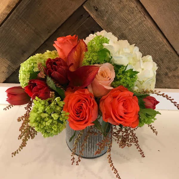 Mixed bouquet of orange, red, white, and green flowers in a metal container