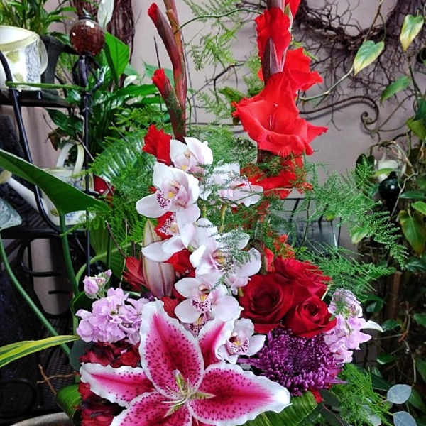 Tall mixed floral arrangement with red roses, pink lilies, and white orchids in a glass vase