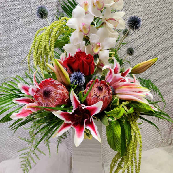 Tall floral arrangement with white orchids, red roses, and pink lilies in a white vase