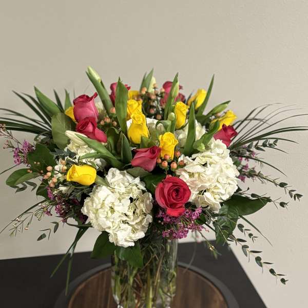 Bouquet of pink and yellow roses with white hydrangeas in a clear glass vase