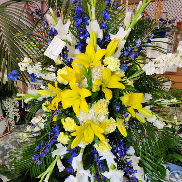 Large standing floral spray with yellow lilies, white blooms, and blue flowers