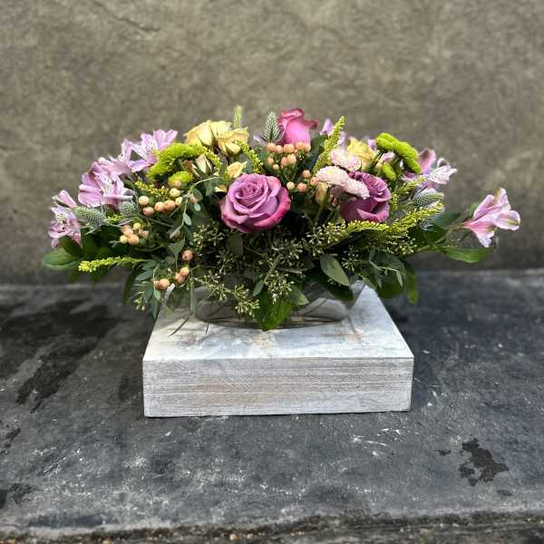 Low floral arrangement with pink and yellow roses in a wooden box