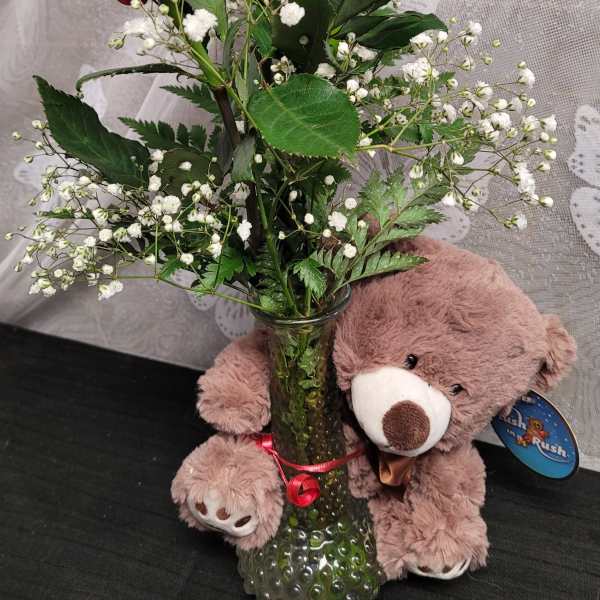 Three red roses in a glass vase with a teddy bear beside it