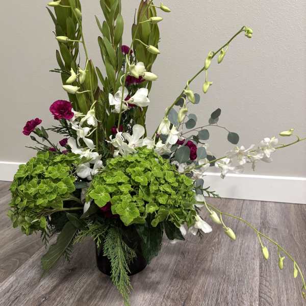 Tall floral arrangement with white orchids, magenta carnations, and green hydrangeas in a black vase