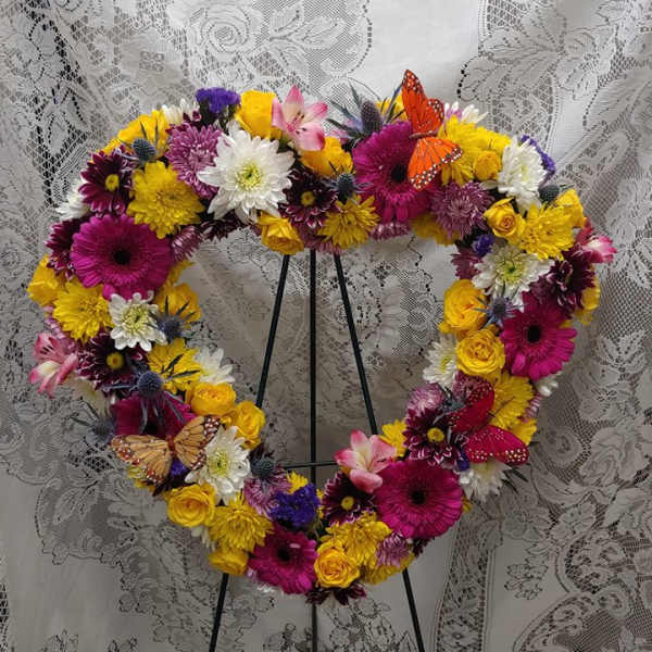Heart-shaped floral wreath with bright mixed blooms on a stand