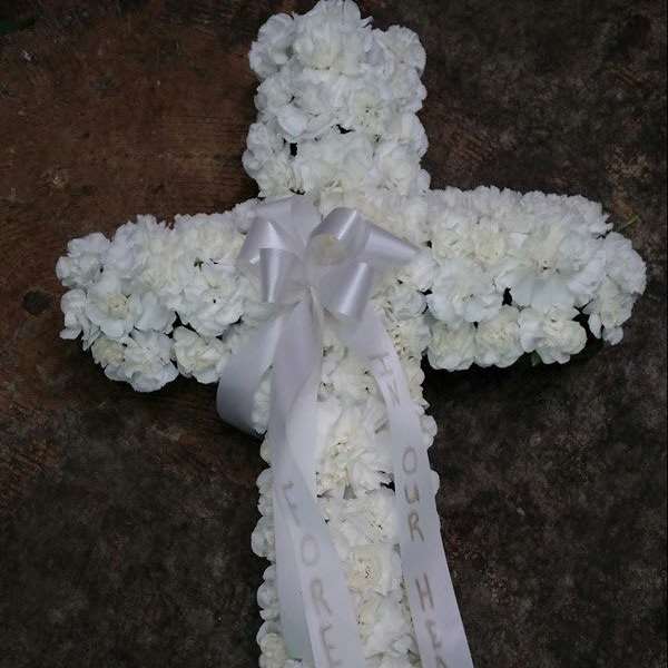 White floral cross with a ribbon bow and hanging memorial ribbons