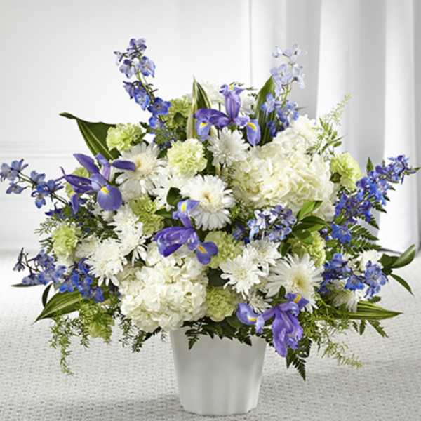 Tall arrangement of white hydrangeas, mums, green carnations and blue irises in a white vase