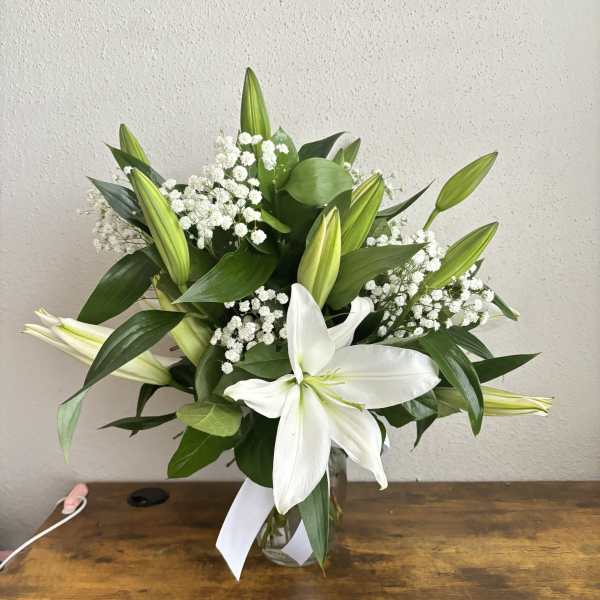 White lilies and baby's breath in a glass vase with a white ribbon