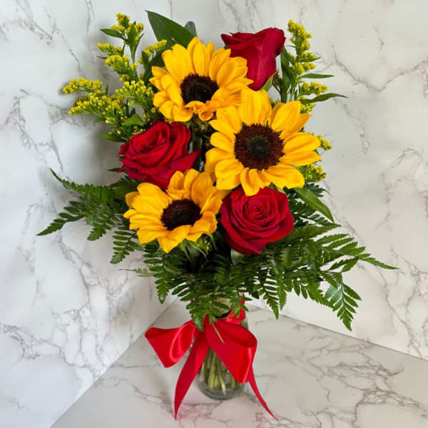 Bouquet of red roses and yellow sunflowers in a glass vase with a red ribbon