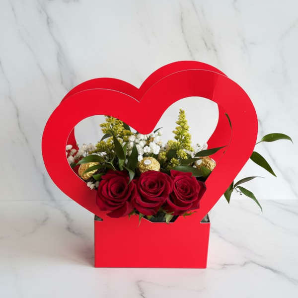 Red roses arranged in a heart-shaped gift box with gold chocolates