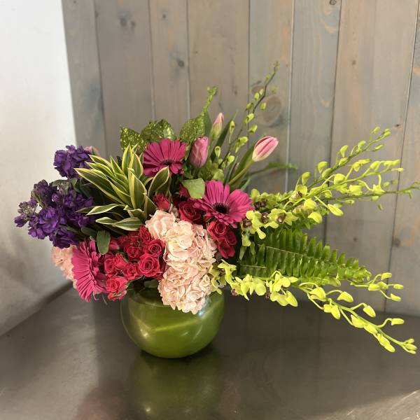 Mixed pink and purple floral arrangement in a green vase