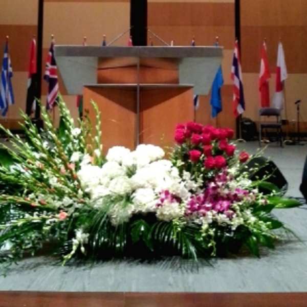Large stage floral spray with white blooms, red roses, and purple orchids arranged in front of a podium