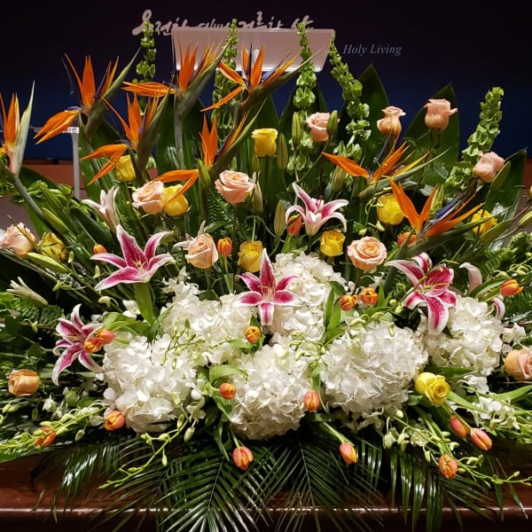 Large altar-style arrangement with white hydrangeas, pink lilies, roses, tulips, and birds of paradise