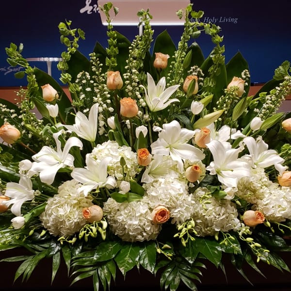 Low, wide arrangement of white lilies, hydrangeas, and peach roses on a stage