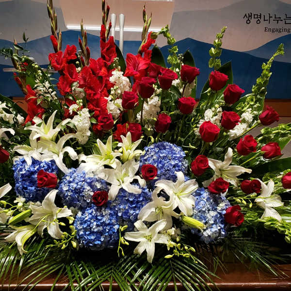 Large red, white, and blue altar arrangement with roses, lilies, hydrangeas, and tall gladiolus.