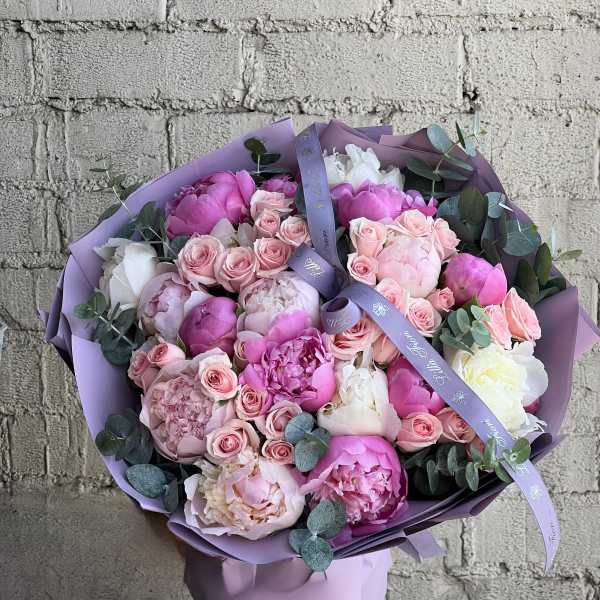 Large round bouquet of pink and white peonies with pale pink roses wrapped in lavender paper and ribbon