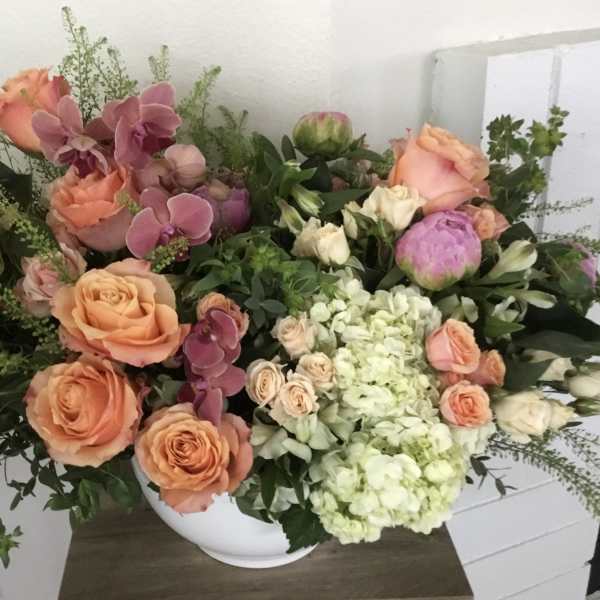 Mixed bouquet of peach roses, pink orchids, and pale hydrangeas in a white vase