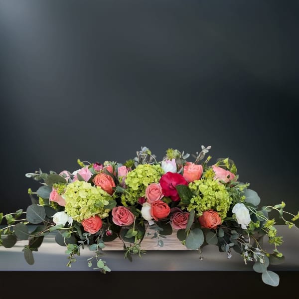 Low floral centerpiece with pink and coral roses and green hydrangeas in a wooden box