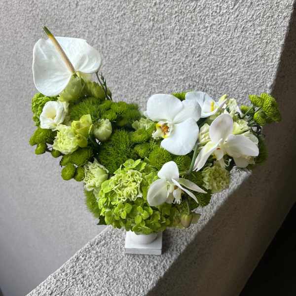 Green and white floral arrangement with orchids and anthurium in a white vase