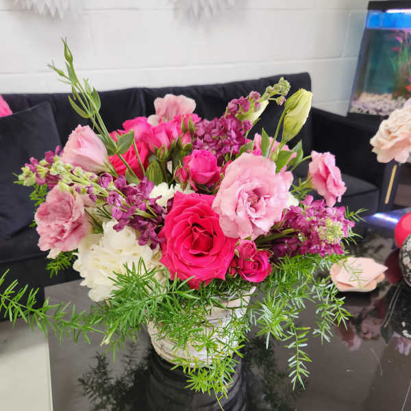 Mixed pink and white flower arrangement with trailing greenery in a white pot on a black table