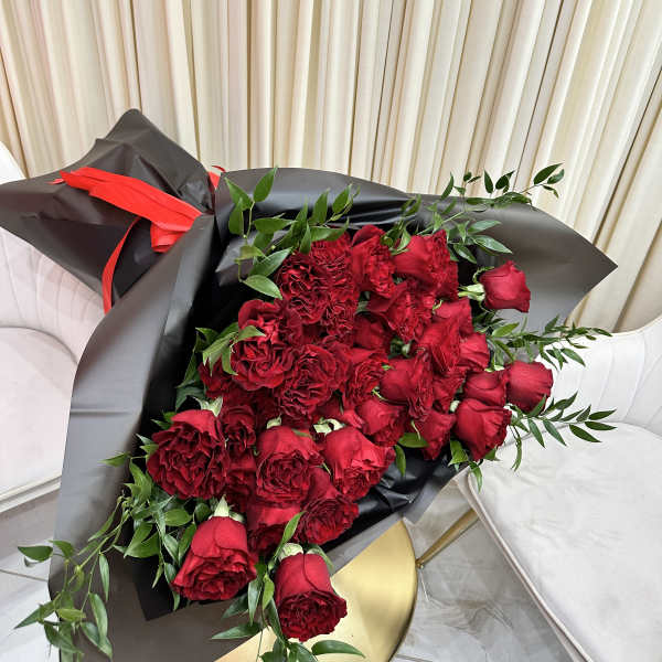 Large bouquet of red roses wrapped in black paper with a red ribbon, resting on a gold table.