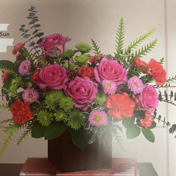 Pink roses and mixed flowers arranged in a square wooden vase