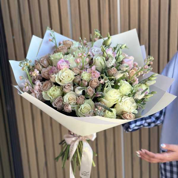 Bouquet of pale roses and pink filler flowers wrapped in cream paper