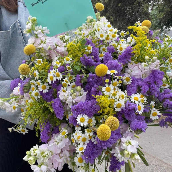 Large bouquet of purple, white, and yellow flowers held with a teal folder