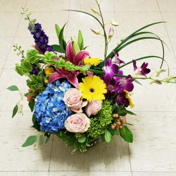 Mixed arrangement of roses, lilies, orchids, gerbera daisies, and hydrangea in a clear glass vase
