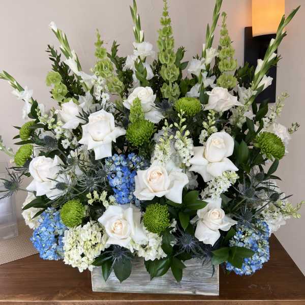 Large floral arrangement with white roses, green blooms, and blue hydrangeas in a wooden box