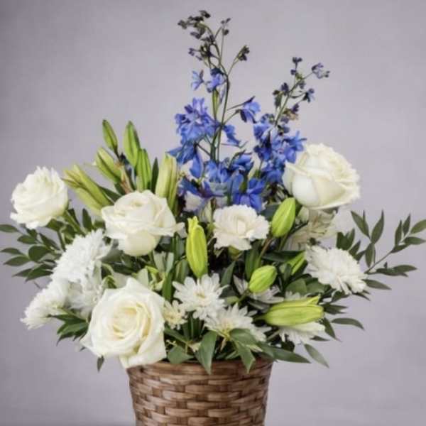 White roses and lilies in a woven basket with blue flowers