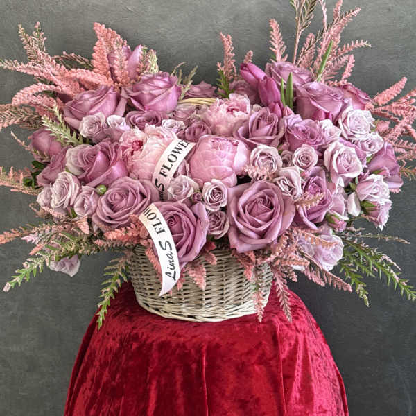 Pink rose arrangement in a wicker basket with ribbon accents