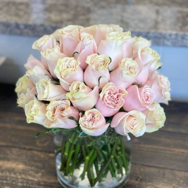 Compact arrangement of pale pink roses clustered in a clear glass cylinder vase