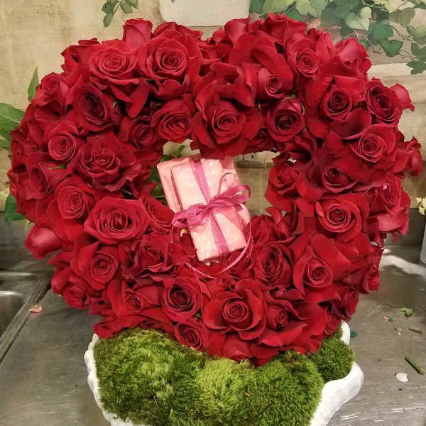 Heart-shaped red rose arrangement with a pink gift box in the center