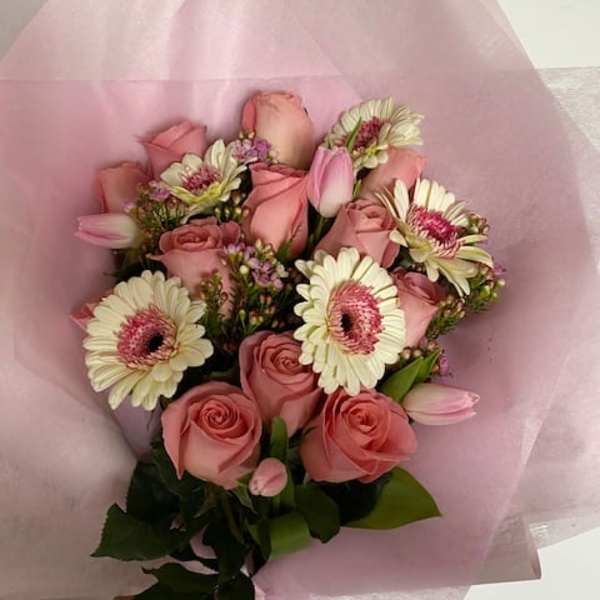 Hand-tied bouquet of pink roses, white gerbera daisies, and tulips wrapped in pink paper