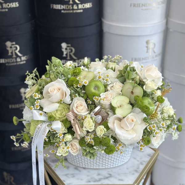 White and green floral arrangement with apples in a white hatbox