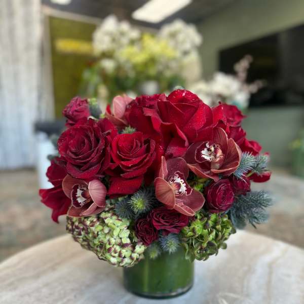 Red roses and burgundy orchids arranged in a green glass vase